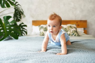 Mutlu gülen çocuk gri yatakta emekliyor, 3.5 aylık bebek gelişim aşamaları.