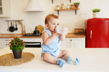 Bebeğim mutfaktaki masada oturuyor ve bebek şişesinden içiyor.