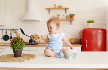 Sevimli erkek bebek mutfak masasında kaşıkla oynuyor.