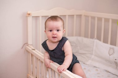 Gülümseyen bebek kameraya bakıyor ve gülümsüyor, yatağında bir çocuk.