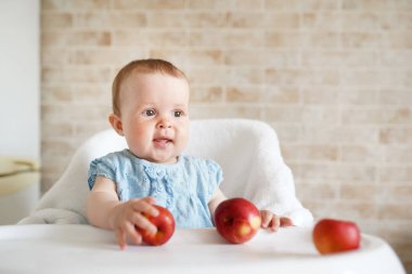 Gülümseyen Bebek meyve yiyor. Küçük kız, güneşli mutfakta beyaz sandalyede oturan sarı elmayı ısırıyor. Çocuklar için sağlıklı beslenme. Bebek için katı yiyecek. Küçük çocuk için atıştırmalık ya da kahvaltı