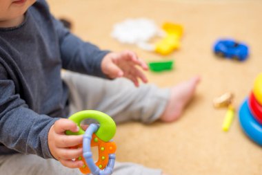 Küçük bebek odada bir sürü renkli oyuncakla oynuyor..