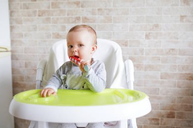Yemek odasındaki sandalyede kaşıklı bebek gülümseyen ve mutlu bir çocuk. Kopyalama alanı olan arkaplan Mutlu çocukluk