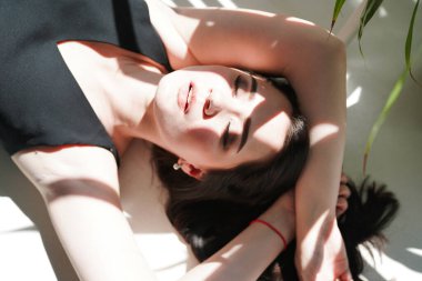 Siyah iç çamaşırlarıyla beyaz, güneşli arka planda yatan şehvetli kadın portresi.