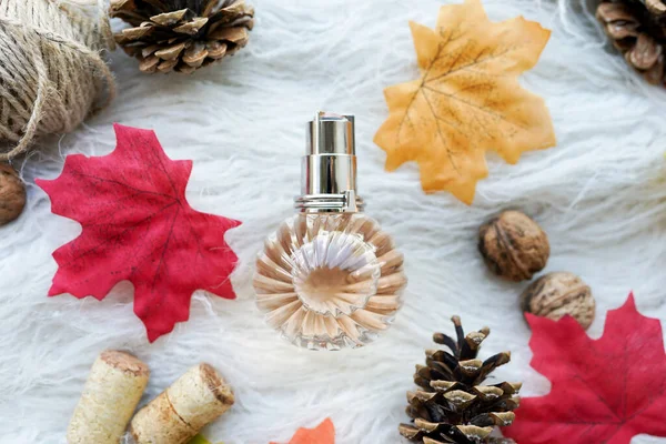 A glass bottle of female perfume laid on white background with autumn yellow leaves. Natural perfumery.