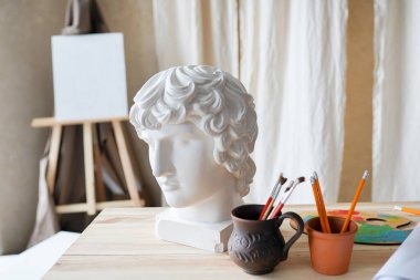Sanatsal fırçalar, kil eski kafa modeli, palet ve çizim malzemeleri. Sanat stüdyosundaki eski ahşap masanın yatay fotoğrafı. Yaratıcı arkaplan