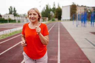 Güzel olgun bir kadın stadyumda koşuyor.
