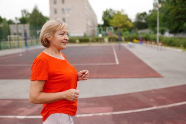 Sabahın köründe koşan yaşlı bir kadın. Çekici görünümlü olgun bir kadın zinde ve sağlıklı..