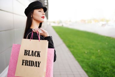 Kara Cuma 'da alışveriş çantalı kadın şehir caddesinde eğleniyor. Siyah elbiseli bir kadın dışarıda yürüyor..