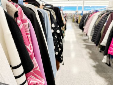 Renkli ceketler ve askılarla dolu bir giyim mağazası koridoru.