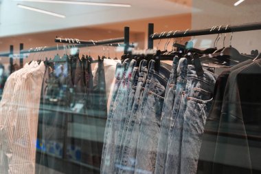 Bir mağazada kot pantolon, gömlek ve ceketlerin siyah askılara asıldığı bir elbise askısı.