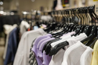 Bir mağazanın içinde düzgün asılmış pastel ve siyah askılı nötr renkli gömleklerle dolu bir elbise rafı.