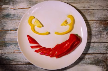 Rustik ahşap masa üstü üzerinde renkli biber dilimlenmiş kırmızı ve sarı tatlı biber, kızgın vegan gelen smiley görüntülemek