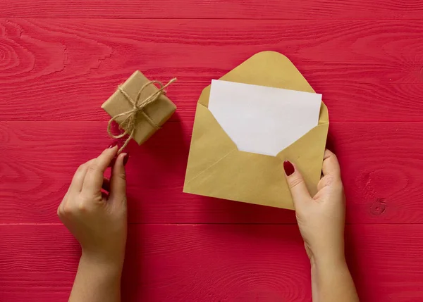 gift and letter of female hands on red wooden background