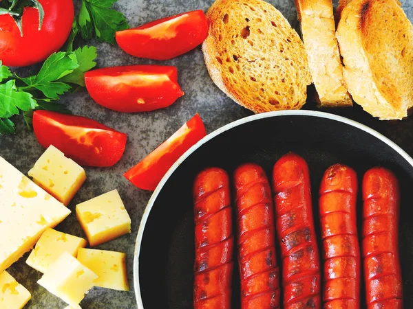 Mini sausages in a frying pan, croutons, cheese and vegetables. Appetizing set with thin mini sausages.