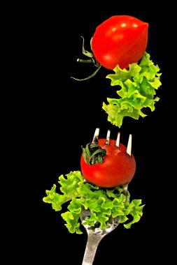 Gıda yükseltebilirim. Bir salata yaprağı ve bir çatal üzerinde bir kiraz domates. Kompozisyon gıda levitation siyah bir arka plan ile. Vegan kavramı.