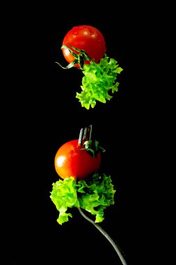 Gıda yükseltebilirim. Bir salata yaprağı ve bir çatal üzerinde bir kiraz domates. Kompozisyon gıda levitation siyah bir arka plan ile. Vegan kavramı.