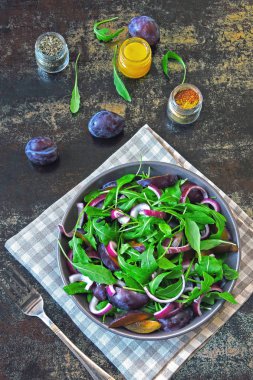 Sağlıklı Roka Salatası, Erik ve mavi şık eski püskü arka plan üzerinde bir kapta soğan. Erik salata bir kase vegan. Erik Roka Salatası. Doğru beslenme kavramı.