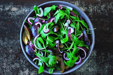 Sağlıklı Roka Salatası, Erik ve mavi şık eski püskü arka plan üzerinde bir kapta soğan. Erik salata bir kase vegan. Erik Roka Salatası. Doğru beslenme kavramı.