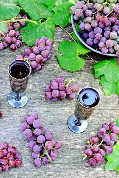 Grape wine in silver glasses. Grapes and grape leaves. The harvest of pink grapes. Still life with wine and grapes.