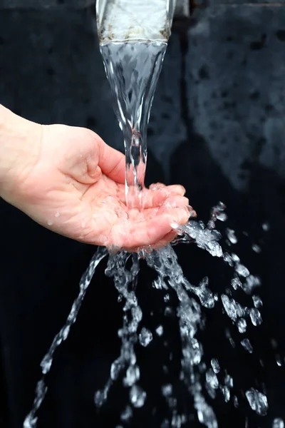 Female hand under a stream of clear water. Splashing water. Cold water source. Drinking water concept.