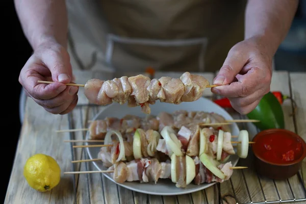 Raw kebabs on wooden sticks are prepared by the chef.