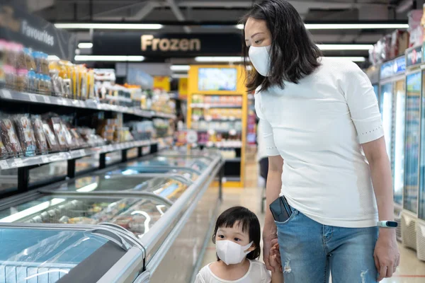 Young asian woman and 2 year old kid with face mask in supermarket. Concept for life in outbreak and new normal.