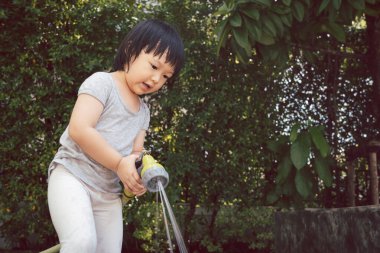 3 yaşındaki Asyalı bir çocuğun bahçe hortumuyla su oynadığı komik bir an. Çocukların yaz ve oyun zamanı için arka plan kavramı.