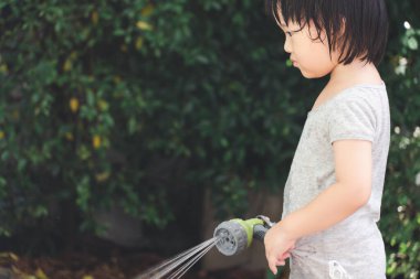 3 yaşındaki Asyalı bir çocuğun bahçe hortumuyla su oynadığı komik bir an. Çocukların yaz ve oyun zamanı için arka plan kavramı.