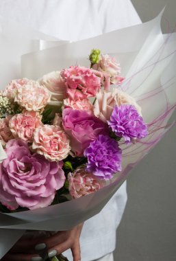 Güzel bir düğün buketi çiçek, farklı renklerde taze güller, bir kızın elinde, gri bir duvara karşı,