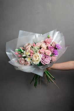 Güzel bir düğün buketi çiçek, farklı renklerde taze güller, bir kızın elinde, gri bir duvara karşı,