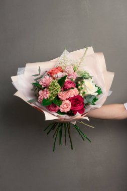 Güzel bir düğün buketi çiçek, farklı renklerde taze güller, bir kızın elinde, gri bir duvara karşı,