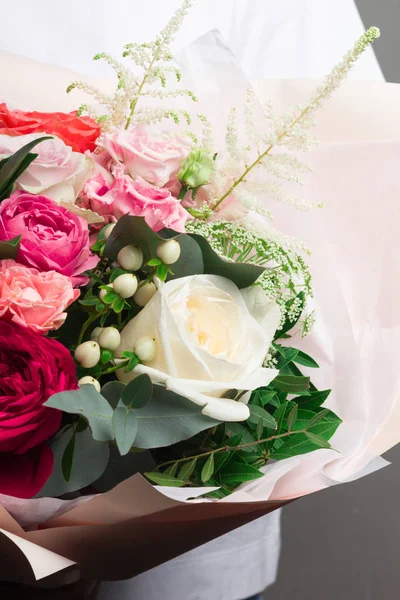 A beautiful wedding bouquet of flowers, fresh roses of different colors, in the hands of a girl, against a gray wall,