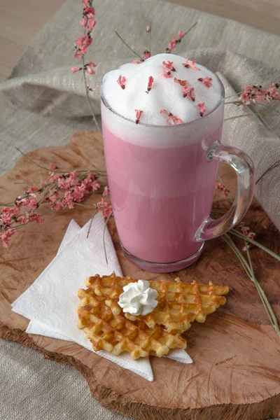 Pink coffee latte macchiato with foamy flowers decorated with sweet waffles baking