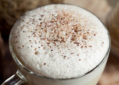 bir bardak kahve, köpüren kapuçino, rendelenmiş çikolata ve tarçın serpilir