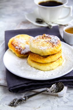 Süzme peynir panckes şeker ve çay gümüş kaşıklar, Beyaz ahşap zemin üzerinde syrniki ile 