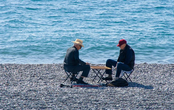Taş bir plajda tavla oynayan iki yaşlı adam