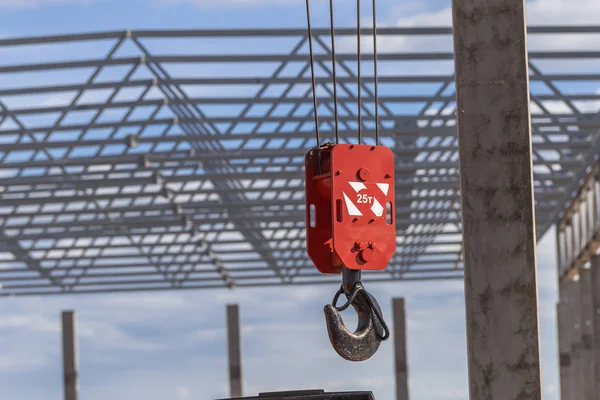 Large red hook of a construction crane against the background of construction farms and the frame of a building under construction