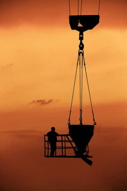 bir işçi ile birlikte bir Beton karıştırıcı bir turuncu günbatımı arka plan üzerinde bir vinç üzerinde yükselir bir inşaat sahasında silüeti