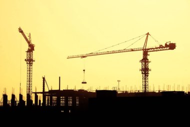 Siluetleri büyük kule vinç inşaat alanının arka plan üzerinde ve hangi arkasında yapı çerçeve bir turuncu günbatımı