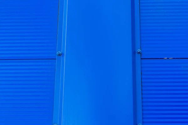 The texture of the wall of the building, made of white and blue sandwich panels. Visible structure of the seam between the panels.