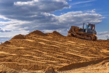 buldozer şantiyede hafriyat işleri yapar, gökyüzüne kadar kum büyük bir dağ tırmıklar