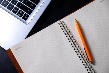 Çalışma alanı geniş bir defter, tükenmez kalem ve bir bilgisayar ile