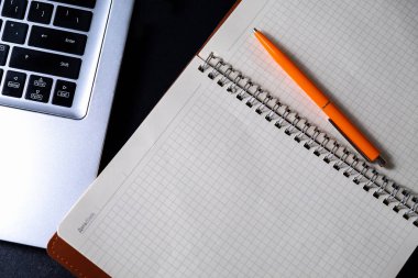 Çalışma alanı geniş bir defter, tükenmez kalem ve bir bilgisayar ile