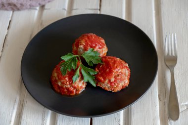 Siyah bir plaka üzerinde üç köfte, domates soslu vardır.