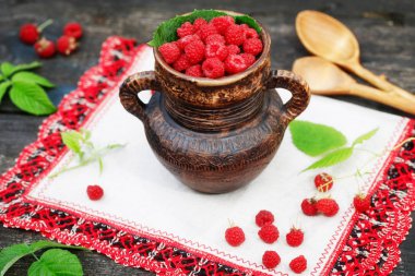 Rustik ahşap zemin üzerine yeşil yaprak ile ahududu seramik kase kavanoz. Yakın, yüksek çözünürlüklü ürün. Hasat kavramı