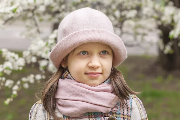 春に咲く木々の背景にライトボンネットの小さな女の子の肖像 — ストック写真