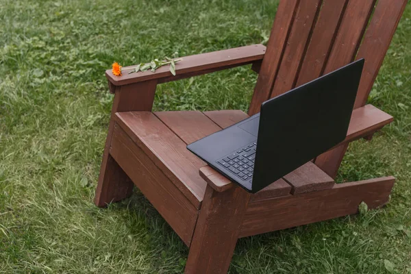 Workplace for remote work in the garden. Laptop on a wooden chair on a background of a garden with trees and flowers