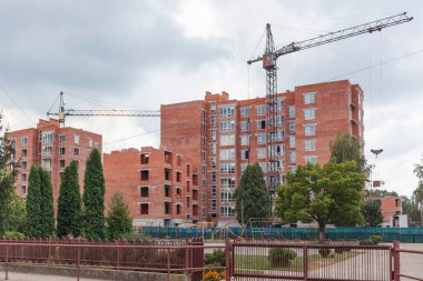 İnşaat alanı ağaçlarla döşenmiş. Çok katlı yeni binaların inşaatı. İnşaat vinci evlerin yanında.