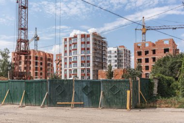 Çok katlı yeni bir binanın inşaatı. Yeşil çitin arkasındaki inşaat alanında..